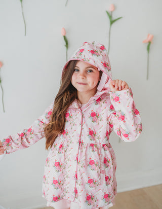 Young girl wearing a pink floral raincoat against a light background with flowers.