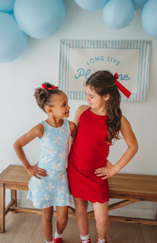 Two young girls in dresses standing next to each other with blue balloons and a decorative sign in the background.