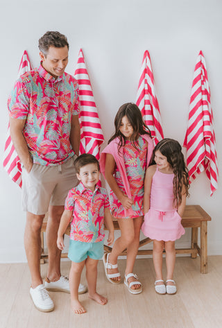 Family of four wearing matching colorful outfits in front of red and white striped towels.