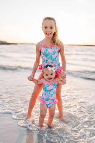 Two young girls in matching swimsuits standing in shallow water at the beach.