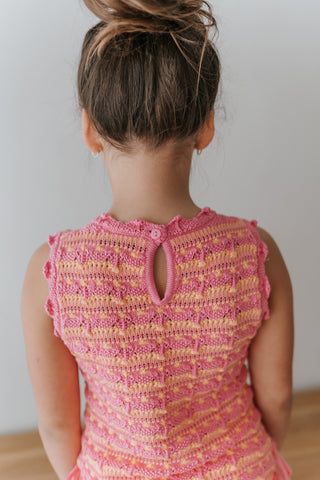 Child wearing a pink and yellow crocheted dress against a plain background