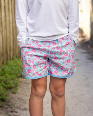 Person wearing light gray long-sleeve shirt and floral shorts on a path with wooden fence.