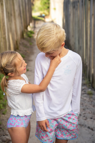 Two children in matching outfits standing close together outdoors.