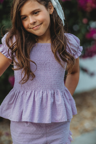 Young girl wearing a purple outfit with a blurred floral background