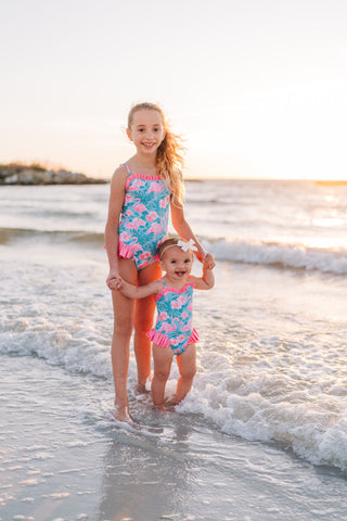 Two children in matching swimsuits standing in the ocean waves.