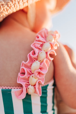 Close-up of a person wearing a pink ruffled swimsuit with a sunlit background