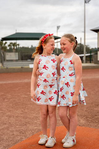Two young girls in matching outfits standing on a baseball field.