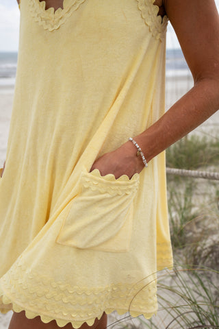 Person wearing a yellow dress with scalloped edges on a beach.