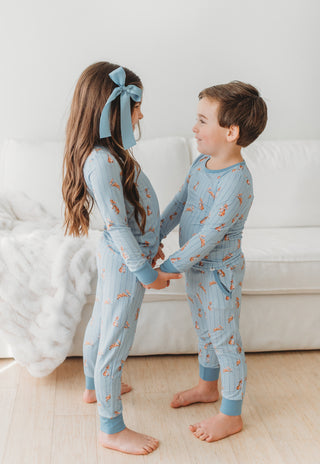 Two children wearing matching blue pajamas with bunnies in a room.
