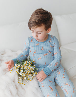 Child wearing blue pajamas with a pattern, sitting on a white surface holding flowers.