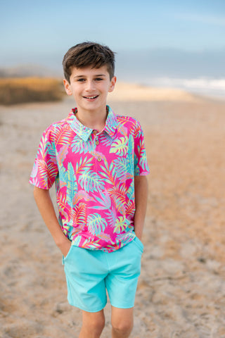 Young boy wearing a colorful shirt and light blue shorts on a beach.