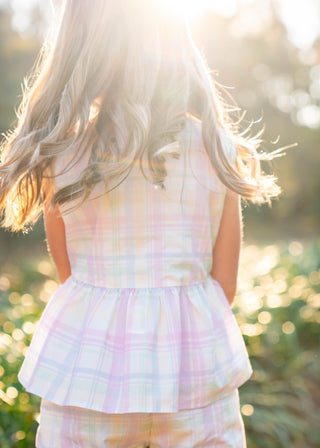 Child wearing a pastel plaid outfit with a blurred natural background