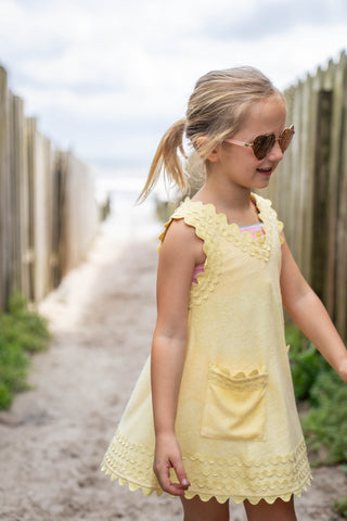 Young girl in a yellow dress standing on a sandy path with wooden fences in the background.