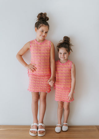 Two young girls wearing matching pink dresses standing against a white wall.