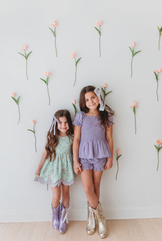Two young girls standing against a wall with floral decorations.