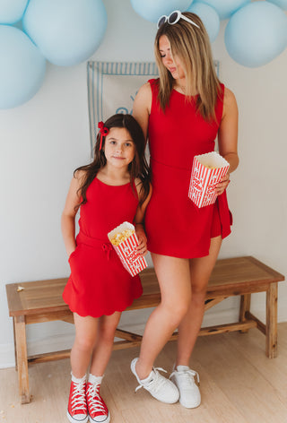 Woman and young girl in matching red dresses with popcorn, standing in a room with balloons.