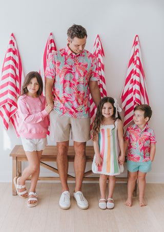Family of four wearing matching pink and white outfits with red and white striped towels in the background.