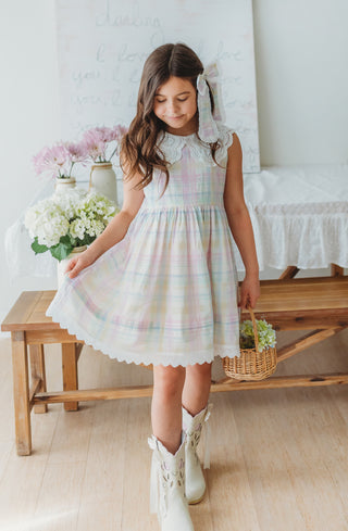 Young girl in a pastel dress standing in a room with flowers and a wooden bench.