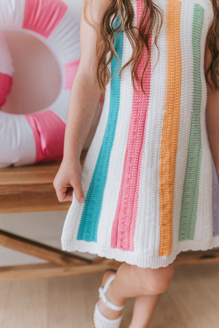 Child wearing a colorful striped dress with an inflatable ring in the background