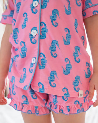 Child wearing pink pajamas with blue seahorse patterns in a bedroom setting.