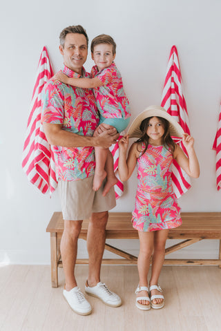 Family of three in matching colorful outfits with beach towels in the background.