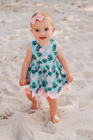 Baby in a floral dress standing on a sandy beach