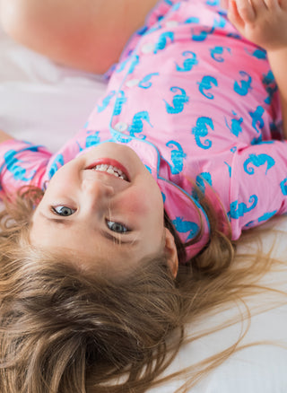 Child wearing pink pajamas with blue seahorse patterns, lying on a white surface.