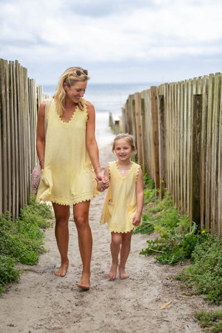Woman and child in matching yellow dresses walking along a sandy path with wooden fences.