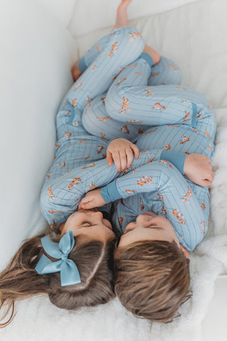 Two children in matching blue pajamas lying on a white surface.