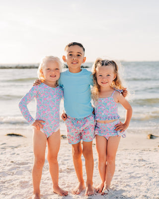 Three children in matching swimsuits standing on a beach.