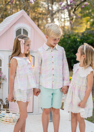 Three children in pastel outfits standing in front of a pink playhouse.