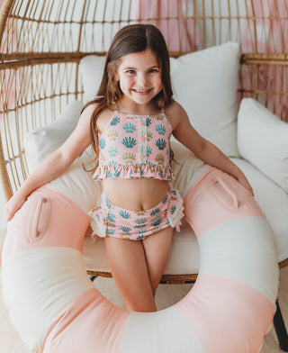 Young girl in a shell-patterned swimsuit sitting on a pink and white inflatable ring.