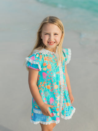Young girl in a colorful dress standing on a beach.