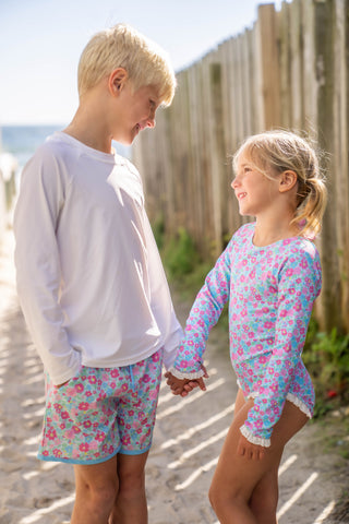 Two children holding hands on a sandy beach with wooden posts in the background.