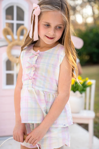 Young girl in a pastel plaid outfit standing outdoors with blurred background