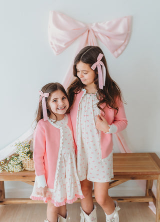 Two young girls in matching outfits with pink ribbons standing in front of a large pink bow.