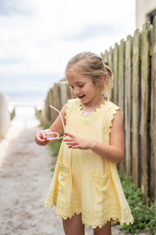 Young girl in a yellow dress standing outdoors near a wooden fence.