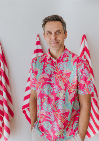 Man wearing a colorful tropical shirt standing in front of red and white striped flags.