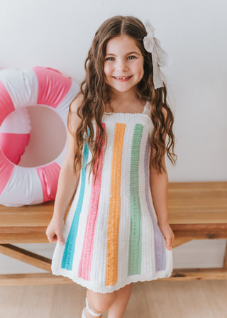 Young girl wearing a colorful striped dress with a pink and white pool float in the background.