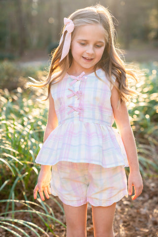 Young girl in a spring plaid outfit standing outdoors with sunlight filtering through.