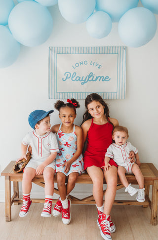 Four children sitting on a bench with blue balloons and a sign in the background.