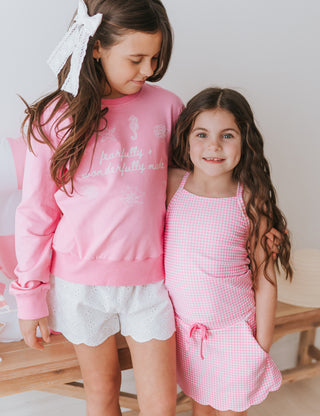 Two young girls wearing pink outfits standing next to each other indoors.