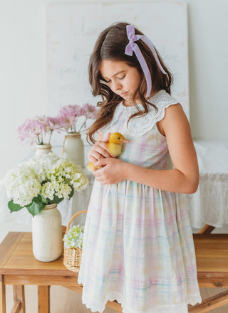 Young girl in a pastel dress holding a duckling in a bright room with flowers and a table.