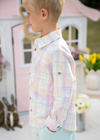 Child wearing a pastel plaid shirt in front of a pink playhouse.