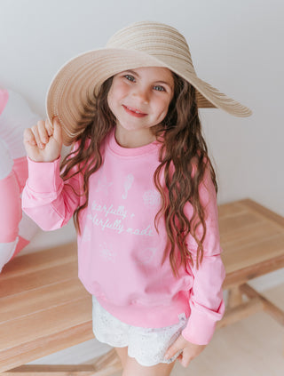 Child wearing a pink sweatshirt and wide-brimmed hat indoors