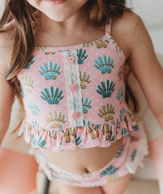 Child wearing a pink top with shell pattern and matching shorts.
