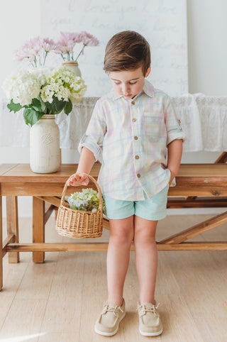 Child wearing pastel plaid shirt holding a basket with flowers in a home setting