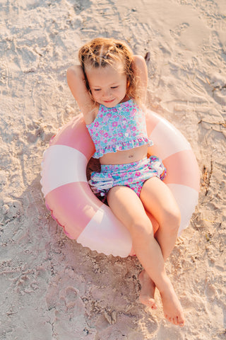 Child sitting on a pink and white inflatable ring on a sandy beach