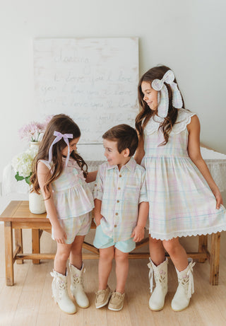 Three children in matching pastel plaid outfits standing together in a bright room.