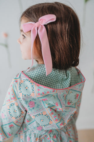 Child wearing a floral rain jacket with a pink headband, standing against a plain background